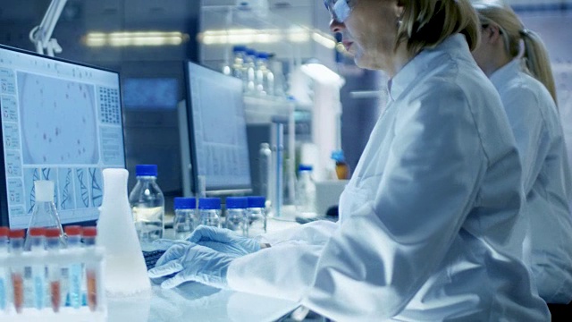 高级女化学师在超现代实验室从事液体化学工作。她和她的同事坐在她的办公桌前，他们在电脑上分析数据。视频素材
