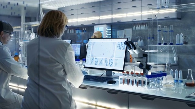 高级女科学家工作与高科技设备在一个现代化的实验室。她的同事们在她旁边工作。视频下载