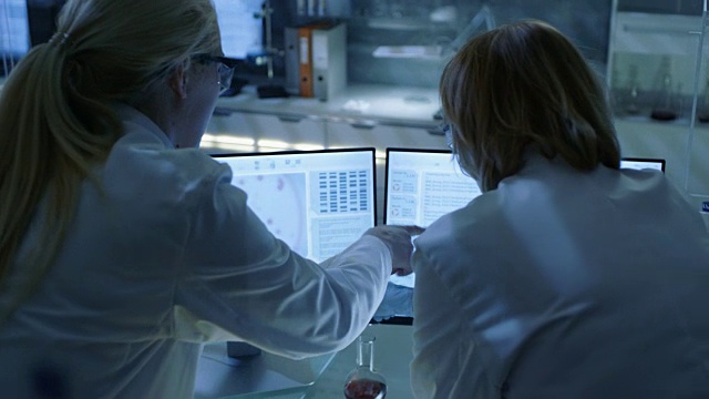 高级女科学家与她的实验室助理讨论科学数据。他们在看一个现代实验室的两个显示器。视频下载