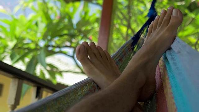 在阳台上的吊床上摆动着男人的光脚。在泰国高涛塔诺特湾度假视频素材