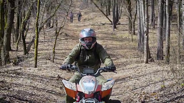 一个男人在保护设备和头盔操作ATV和沿着道路从一边到另一边的特写。极限旅游爱好者在道路上骑四轮自行车，背景中有人视频下载