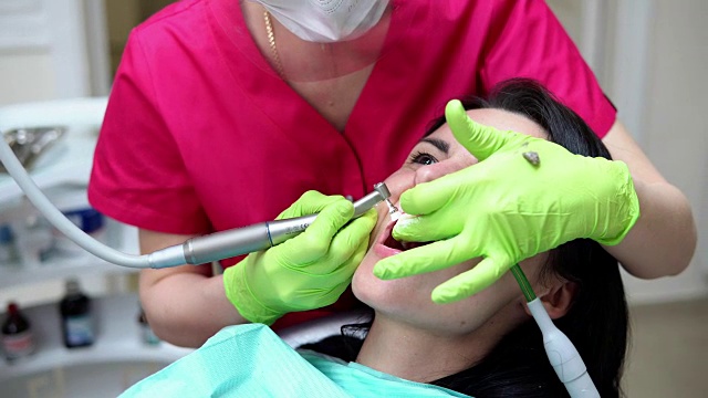 牙医用专业牙膏和自动牙刷清洁妇女的牙齿。牙科医生使用唾液喷射器或牙科泵排出唾液。视频下载