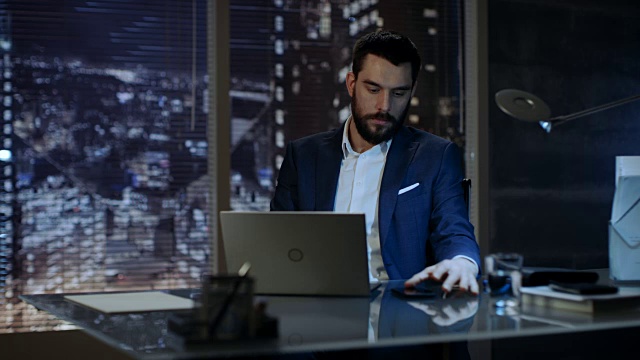 一个商人在他的私人办公室里用笔记本电脑工作，可以看到大城市的窗户。视频素材