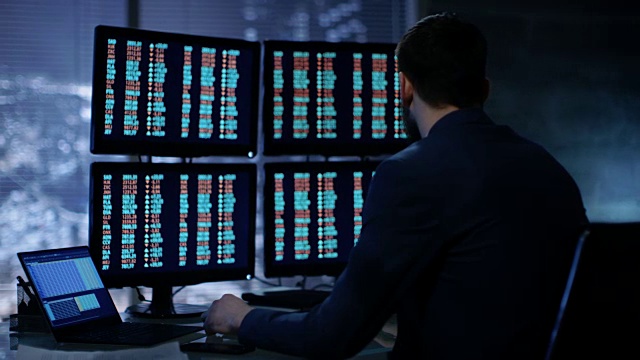 深夜交易员在他的多个股票信息显示器上读取数字。在背景大城市窗口视图。视频素材
