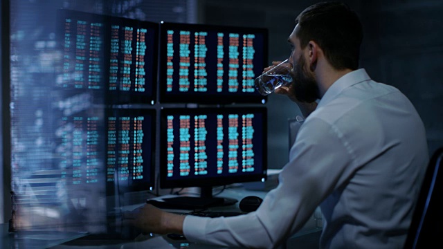 深夜交易员在他的多重显示器上读取股票信息的数字。在背景大城市窗口视图。视频素材