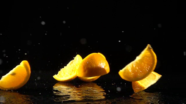 橙色的水果片落在黑色的背景上，慢动作视频素材