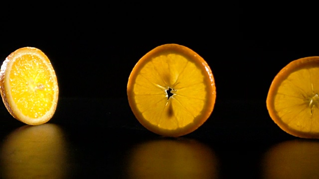 滚动的橙色水果片在黑色的背景，慢动作视频素材