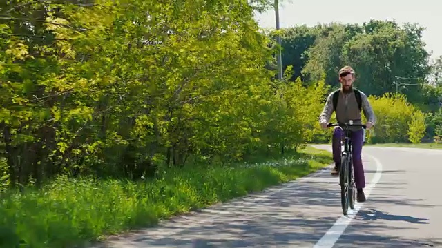 一位留着胡子的帅哥沿着自行车道骑自行车。在一个晴朗的春日。替身拍摄视频素材