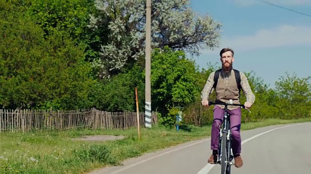 一个留着胡子的年轻人正在骑自行车。在一个晴朗的春日享受一次旅行。替身拍摄视频素材