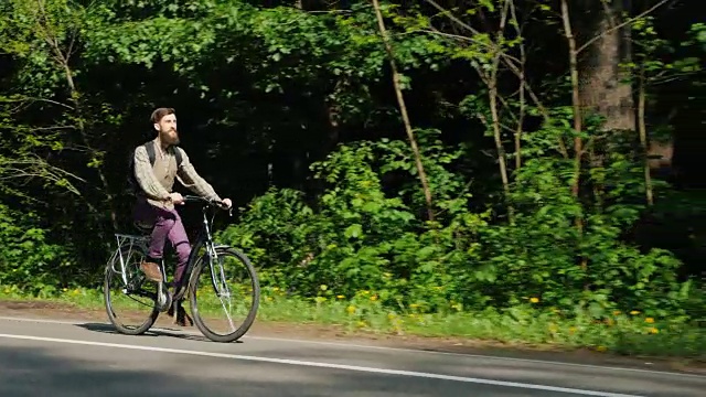 倾斜稳定器拍摄:一个骑自行车的人出现在空的框架。他骑自行车，背景是一片绿色的森林。良好的春天视频素材