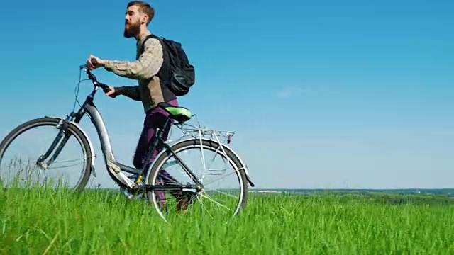 生态旅游——一个人骑着自行车穿过绿色的草地，映衬着湛蓝的天空。田园诗般的风景，环保的地方视频素材