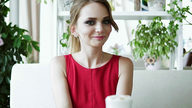 漂亮的年轻女子，金色长发在红色组合坐在咖啡馆与晚和等待某人。Slowmotion拍摄视频素材