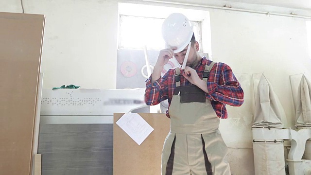 一个穿着细木工制服的年轻木匠，头上戴着一顶白色的头盔。视频素材