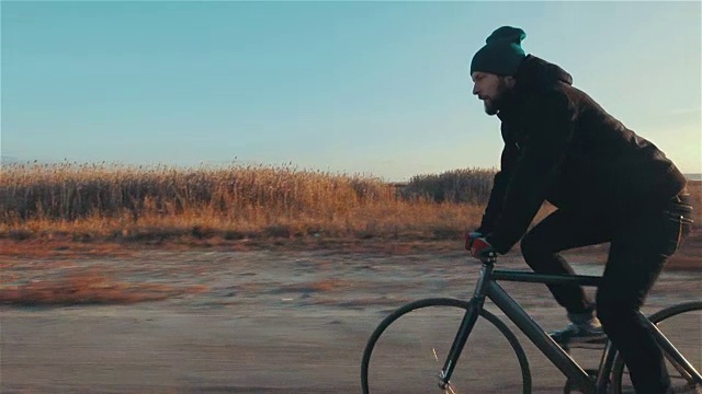 年轻英俊的潮人骑固定齿轮自行车在日落，户外视频素材