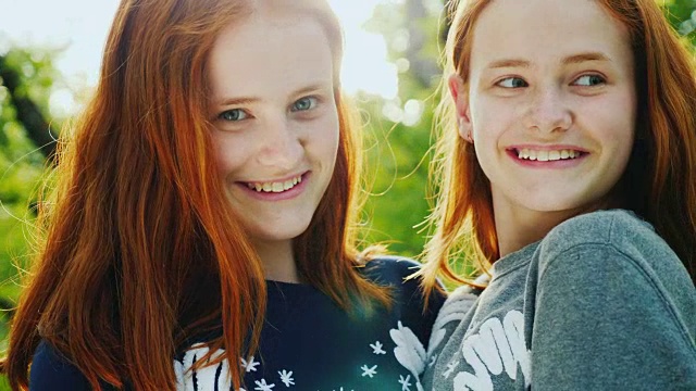 快乐双胞胎姐妹的肖像。微笑着，看着阳光下的相机。可爱的红发少女视频素材