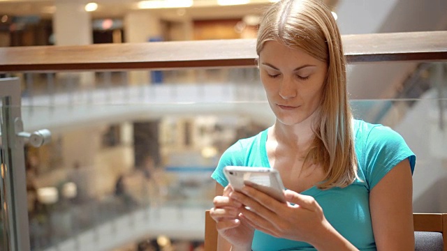 女人坐在商场广场上用手机浏览，看新闻，和朋友聊天视频下载