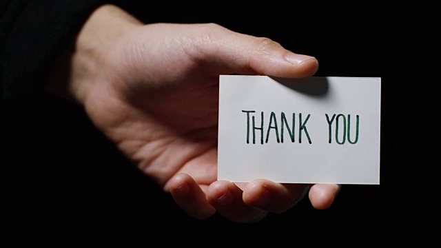 一只手展示一张卡片，上面写着:“谢谢你”。经营理念，谢谢，记录网站。视频素材