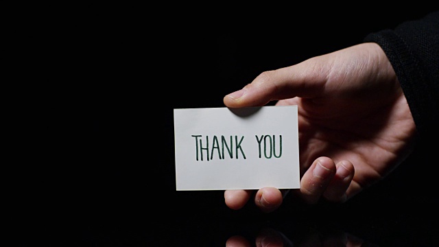 一只手展示一张卡片，上面写着:“谢谢你”。经营理念，谢谢，记录网站。视频素材