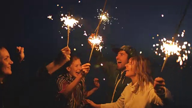 一群年轻的朋友在海滩聚会。朋友们在夕阳下用烟花跳舞庆祝视频素材