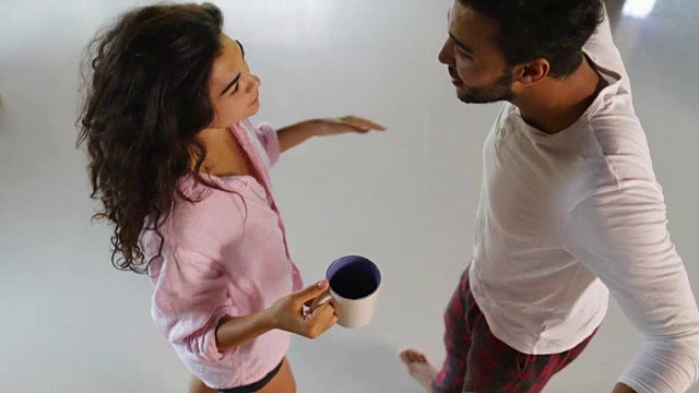 快乐的夫妇在早晨跳舞在顶角的观点，年轻愉快的男人和女人拿着杯与咖啡在现代公寓工作室视频素材