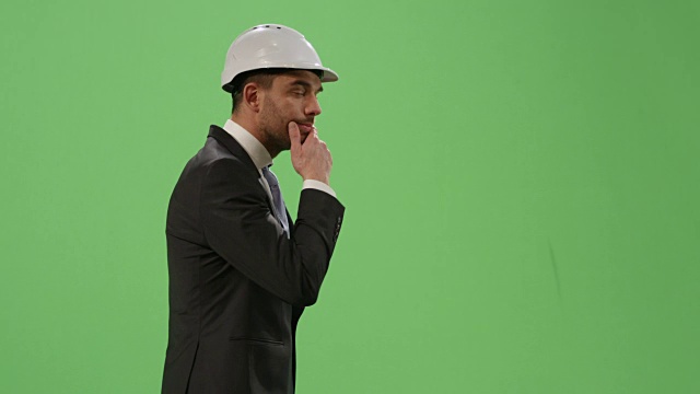 商人戴着安全帽，穿着西装，走在绿色屏幕模型的背景。视频素材