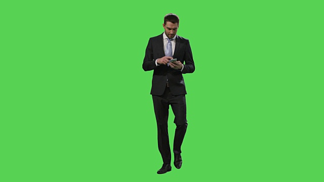 一名西装革履的商人正在用智能手机行走，背景是一个绿色屏幕模型。视频素材