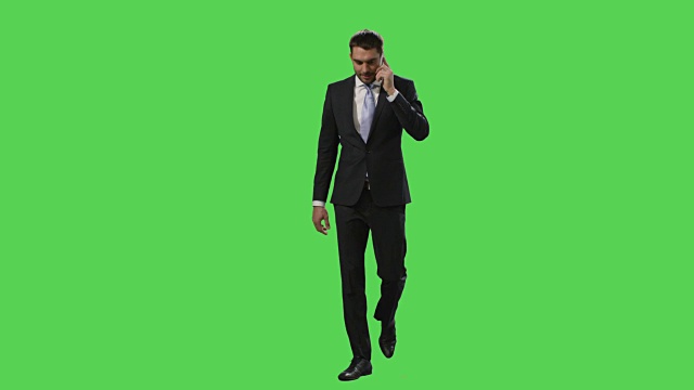 一个穿着西装的商人正在一边走路一边用手机打电话，背景是一个绿色的模拟屏幕。视频素材
