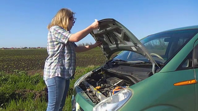 一个戴眼镜、穿着格子衬衫的女孩手里拿着一张餐巾，打开了汽车的引擎盖。一个女人在一辆破车里视频下载