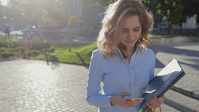 年轻漂亮的女商人，穿着蓝色衬衫，在城市的休息时间使用现代智能手机，职业女性雇主在外面用手机发短信视频素材