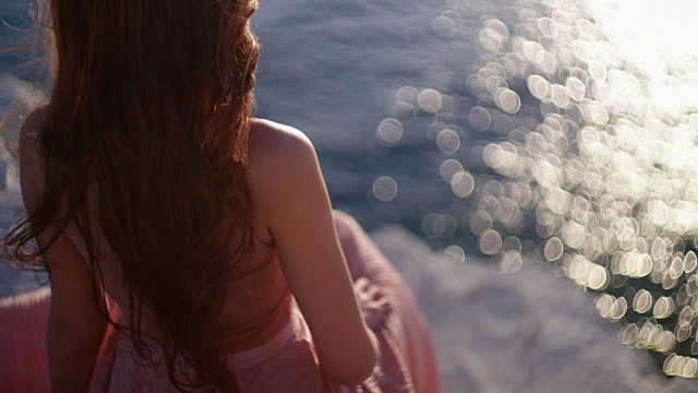 年轻的红发女郎坐在岩石上望着大海视频素材
