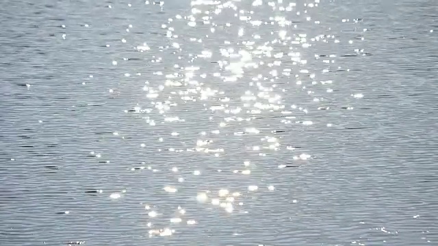 阳光洒落在浅蓝色的水面上，四周环绕着金色的散景视频素材
