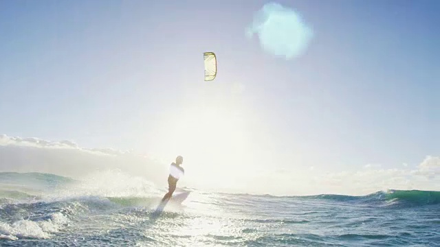 日落时分，一名年轻人在蓝色的海洋中骑着冲浪板风筝冲浪视频素材