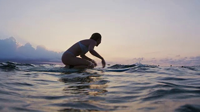 穿着比基尼在冲浪板上划水的漂亮年轻女子视频素材