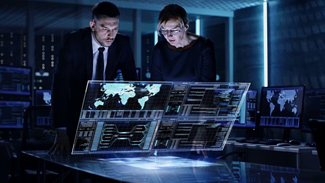 男女政府人员在满是电脑和动画屏幕的大监控室使用触屏互动3D面板。视频素材