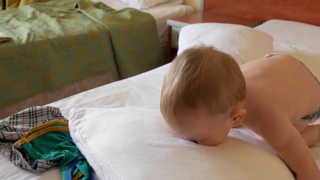 可爱的学步男孩在床上玩枕头和笑。他把它扔了出去，倒在它旁边视频下载