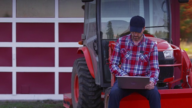 Farmer坐在拖拉机上使用笔记本电脑视频素材