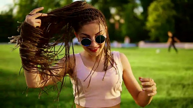 年轻漂亮的女孩带着恐惧在公园跳舞。在阳光明媚的日子里，穿着牛仔裤戴着墨镜听着音乐跳舞的漂亮女人。Slowmotion射杀。视频素材