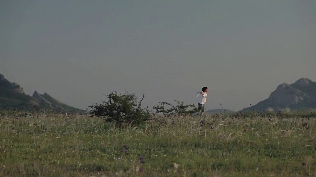 一个拿着手帕的男孩在群山的背景下跑着视频素材