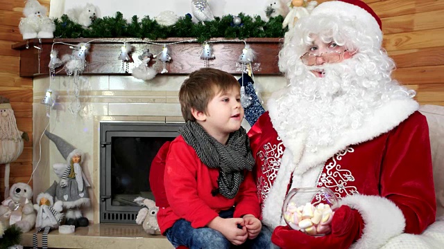 小男孩坐在圣诞老人的腿上，孩子拜访圣诞老人的冬季住所，告诉他的愿望视频素材