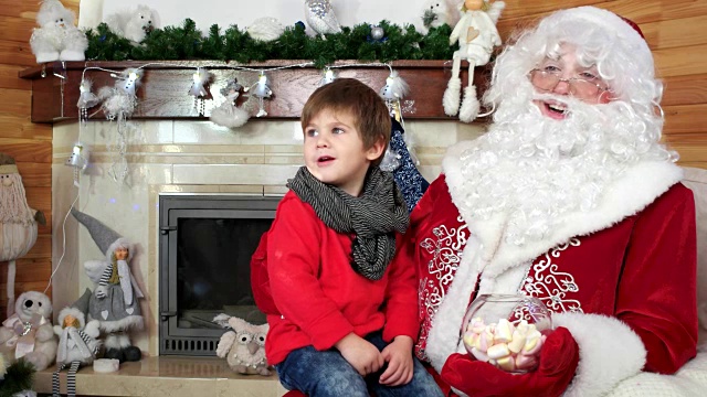 小男孩坐在圣诞老人的腿上，孩子告诉圣诞老人他的圣诞愿望，节日气氛视频素材