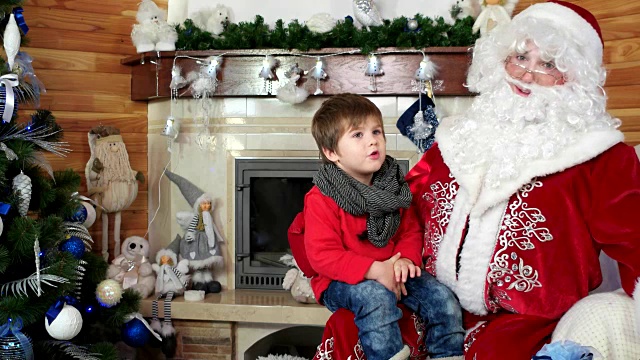 小男孩坐在圣诞老人的腿上，孩子告诉爸爸诺埃尔他的圣诞愿望，大礼物给听话的孩子视频素材