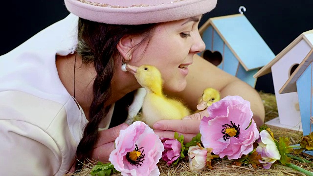 画像，一个漂亮的年轻女子，梳着两条辫子，戴着一顶有趣的粉红色帽子，正在玩黄色的小鸭子。带有主题装饰的工作室视频视频下载