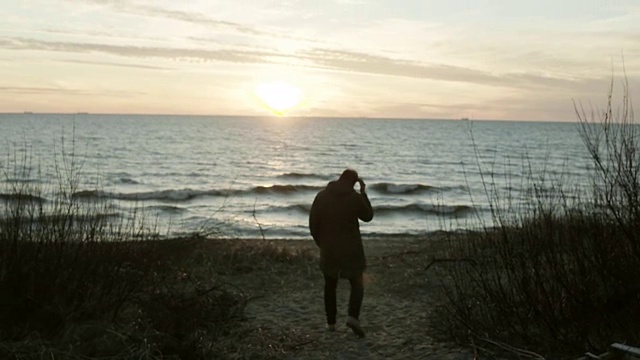 一个年轻人在日落时走在海边的背影。孤独的男性在寒冷的日子里独自在海滩上度过时光视频素材