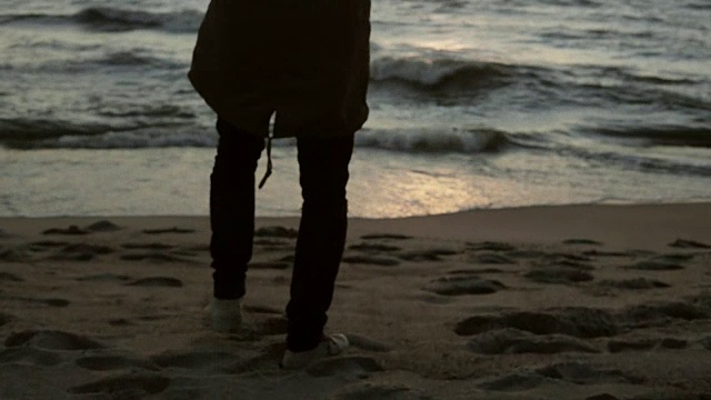 一个孤独的人走在海边，欣赏着夕阳。年轻的雄性欣赏着海滩上的波浪视频素材