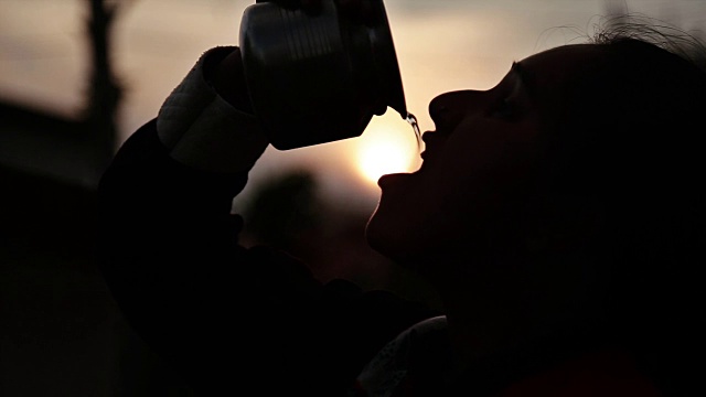 日落时女孩喝水的剪影。视频素材