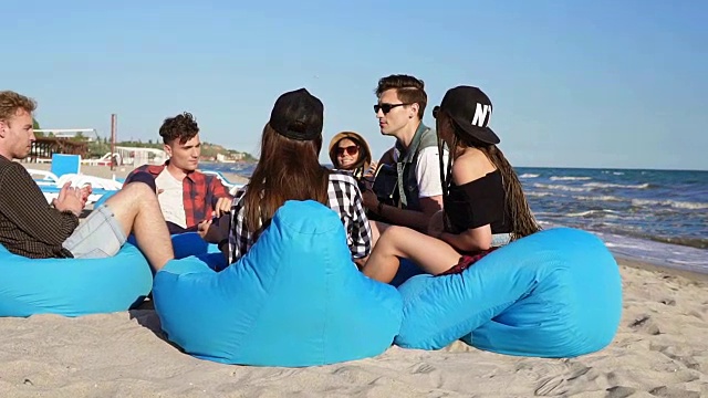 一群朋友坐在沙滩上的安乐椅上弹吉他，在一个夏天的晚上唱歌。Slowmotion拍摄视频下载