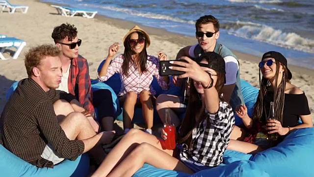 一个年轻的潮女在一个夏天的晚上给一群朋友拍视频或者自拍，他们坐在沙滩上的安乐椅上，弹吉他或者唱歌。Slowmotion拍摄视频下载