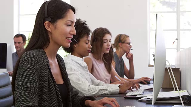 一排女人在一个开放式办公室里使用耳机视频素材