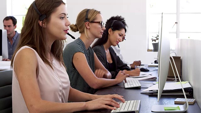 三个女人戴着耳机在办公室的电脑前工作视频素材