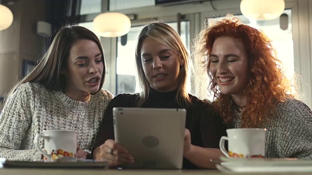 在咖啡馆里，年轻快乐的女人一边用触控板聊天一边大笑。视频素材